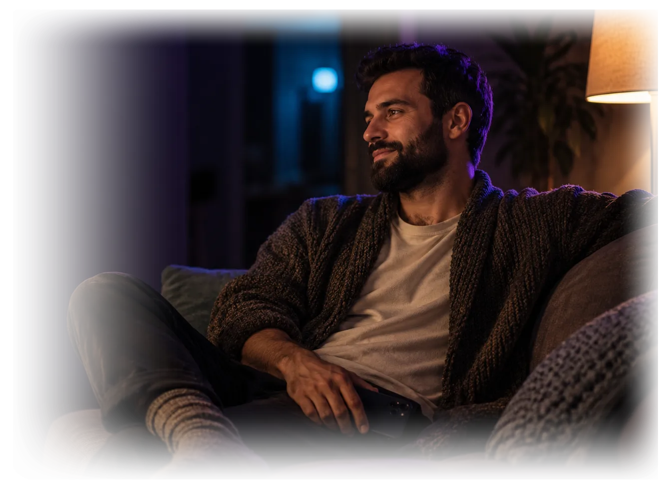 Ein Mann sitzt abends entspannt auf dem Sofa, das Handy locker in der Hand und mit dem Bildschirm nach unten.